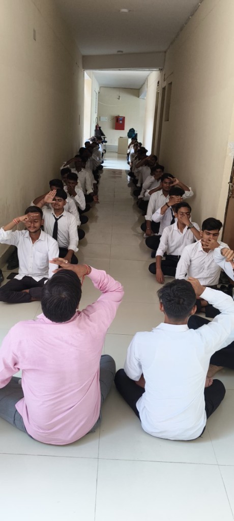 Male students seated in rows practicing Anulom Vilom in a brightly lit hallway on International Yoga Day